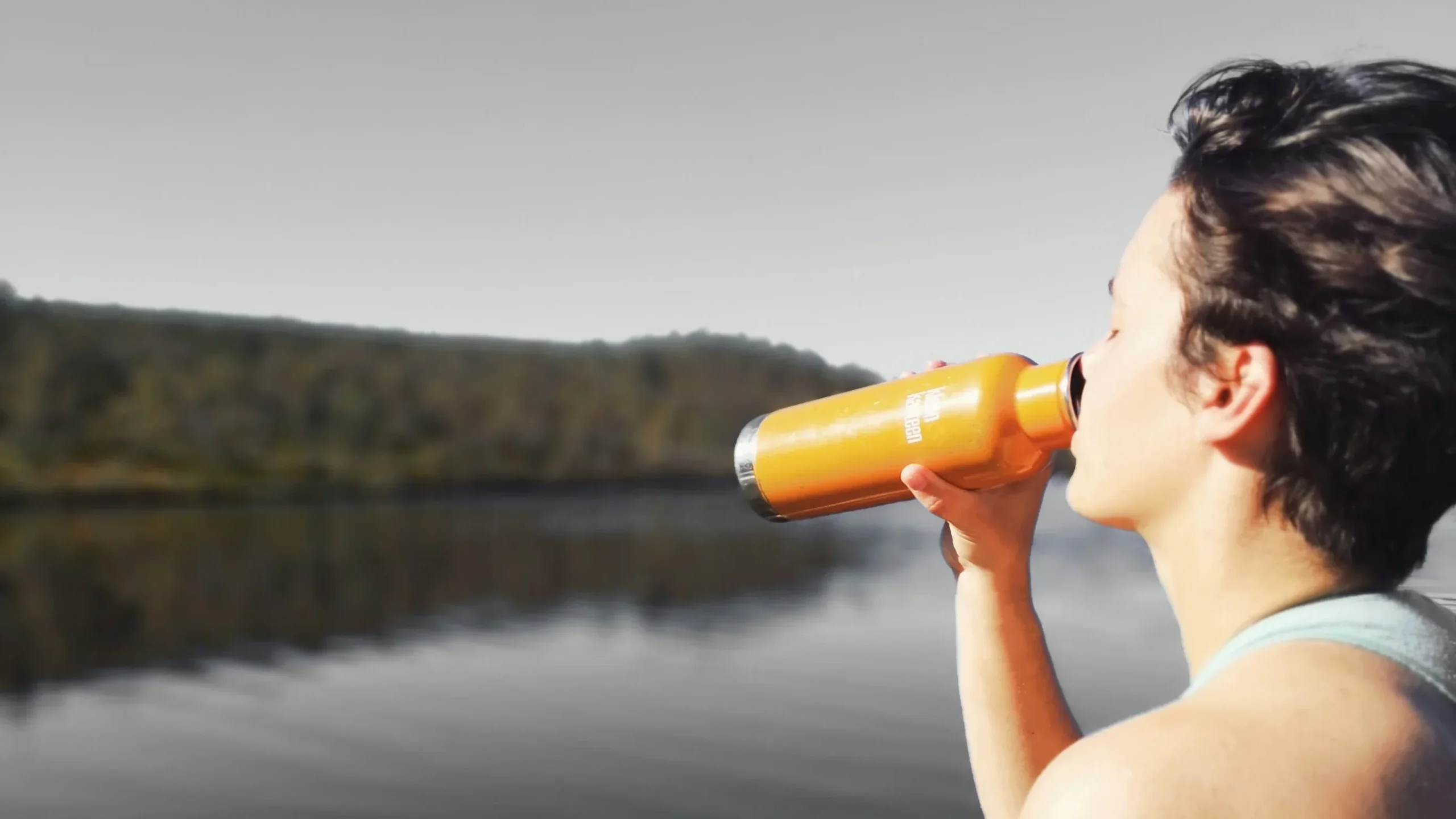 Personne buvant de l'eau dans sa gourde face à un lac